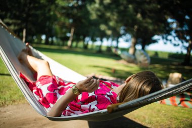 Young woman resting in a comfortable hammock in a green garden on sunny day.