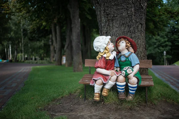 A cute doll statues boy and girl sitting on a bench with feeling on a happiness on the morning atmosphere in the garden