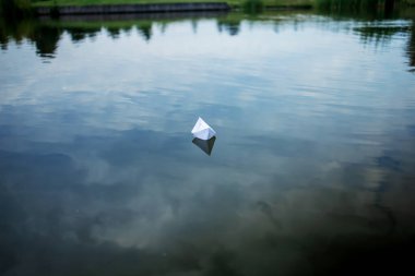 White paper boat sailing on blue water surface of lake.