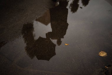 Su birikintisindeki şemsiyenin yansıması, ıslak asfalt doğal arka plan. Yağmur mevsimi. Boşluğu kopyala