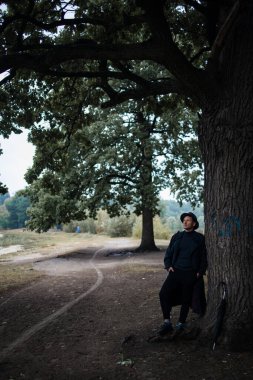 Yağmurlu ormanlarda gezen şık ceketli ve siyah şapkalı genç bir İngiliz.