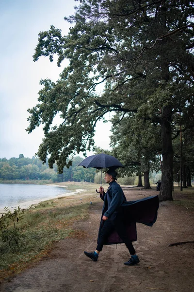 young english man in stylish vintage coat and black hat walking in rainy forest