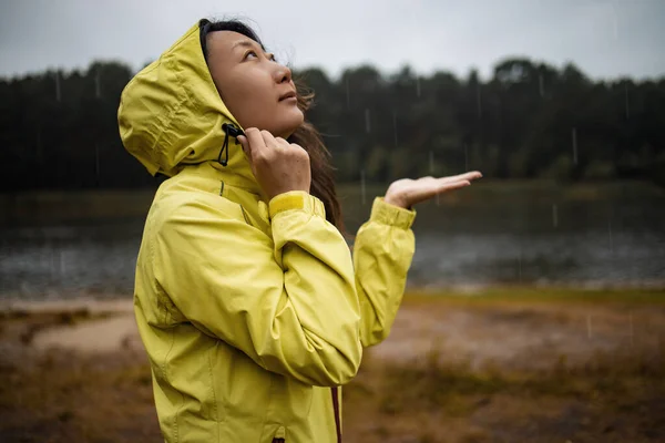 Asian woman With Yellow Rain Coat in forest. Girl enjoying rainy fall day looking up at sky