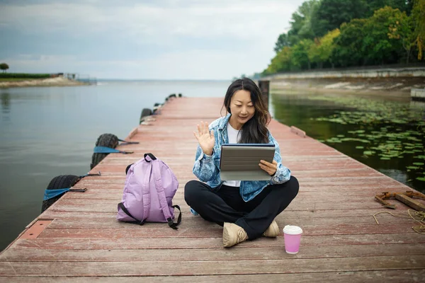 Beautiful traveler asian girl using tablet at wooden bridge. young girl tourist with laptop sitting in port.