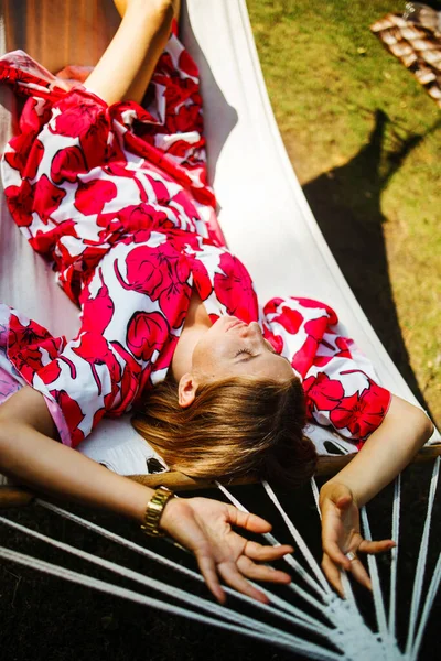 阳光明媚的日子里 金发碧眼的年轻女子躺在一个绿色花园里舒适的吊床上 — 图库照片