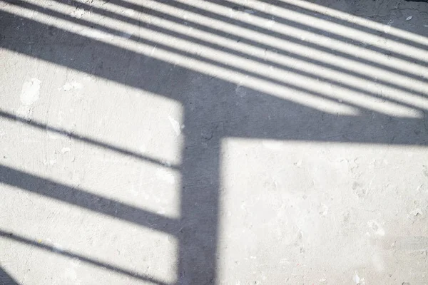 The sun is casting railing shadow over the white concrete wall and floor.