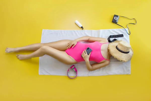 身穿粉色泳衣耳机的年轻女子的头像是用黄色背景的毛巾听音乐 海上休息 晒黑的概念 — 图库照片