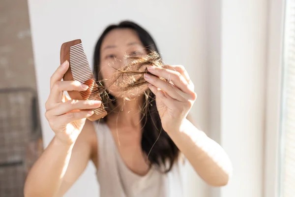 Asian girl with comb and problematic hair on a white background, hair loss concept.