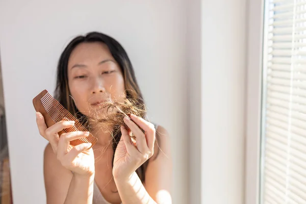 Asian girl with comb and problematic hair on a white background, hair loss concept.