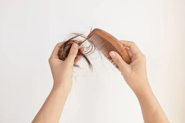 Females hands clean the comb from fallen hair. Close up. White background. Concept of hair loss, baldness and hair care