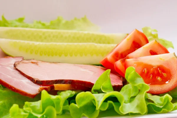 yeşil salata, salatalık ve domates ile bir plaka üzerinde sulu domuz pastırması.