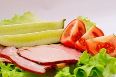 yeşil salata, salatalık ve domates ile bir plaka üzerinde sulu domuz pastırması.