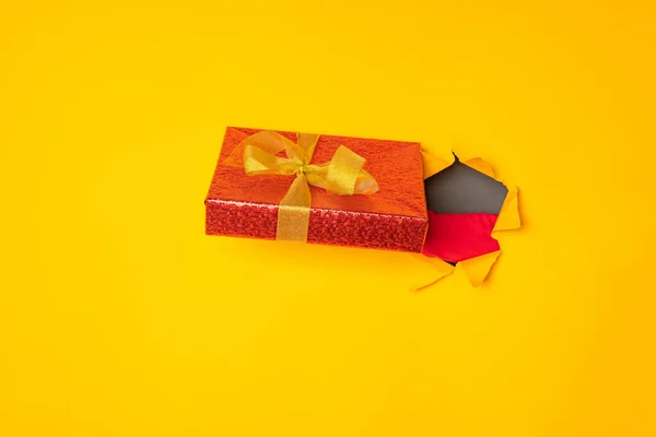 Santa\'s hand holding a box with a gift in the hole yellow background