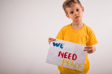 Beyaz duvarın yanında duran ve elinde kağıt tutan çekici küçük bir çocuk.