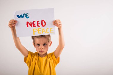 Beyaz duvarın yanında duran ve elinde kağıt tutan çekici küçük bir çocuk.