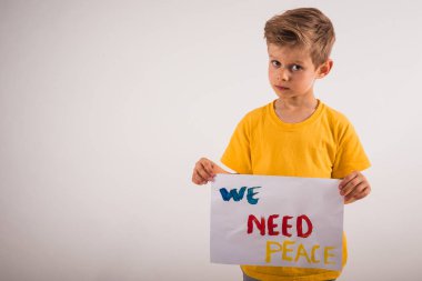 Beyaz duvarın yanında duran ve elinde kağıt tutan çekici küçük bir çocuk.