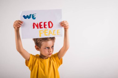 Beyaz duvarın yanında duran ve elinde kağıt tutan çekici küçük bir çocuk.