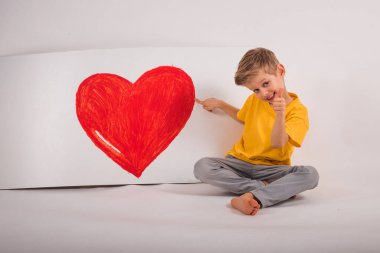 Mutlu çocuk yerde oturuyordu. Onun yanında büyük bir kırmızı var. 