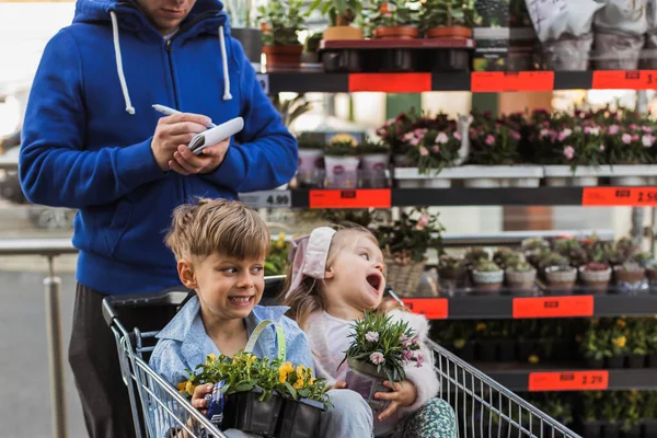 屋外の花の間に鉢植えの植物を持つ幸せな男の子と女の子 — ストック写真