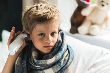 Suçiçeği olan çocuk yatağında oturmuş, ateşi ölçüyor..