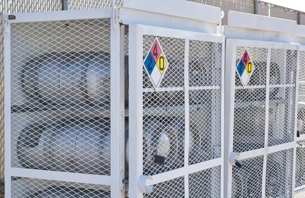 Houston, Texas USA 09-18-2022: Liquid Petroleum gas cylinders stored horizontally in metal safety cages with chemical hazard signs, eye level angle view.