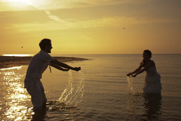 Active couple jumping into water on sunset — Stock Photo, Image