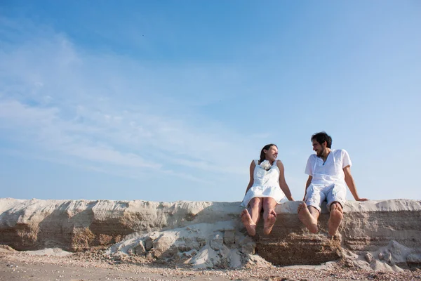 Young couple sitting on the beach with your feet and laughing — Stock Photo, Image