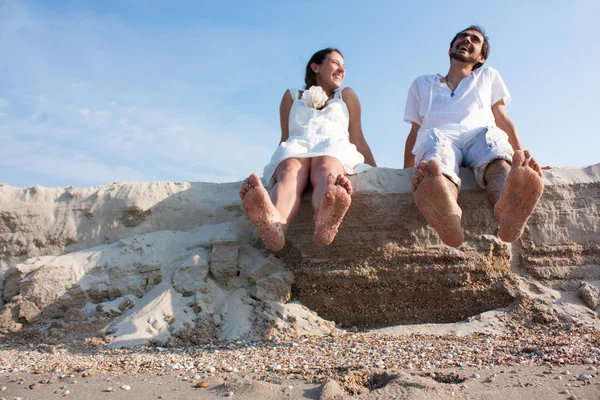 Young couple sitting on the beach with your feet and laughing — Stock Photo, Image