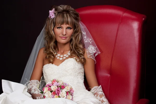 blonde bride sitting in a red chair in the studio on a black background