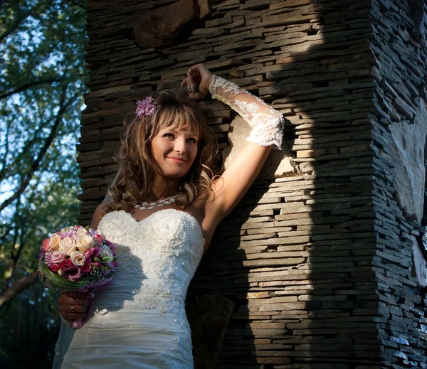 Belle mariée avec bouquet près du mur de pierre — Photo
