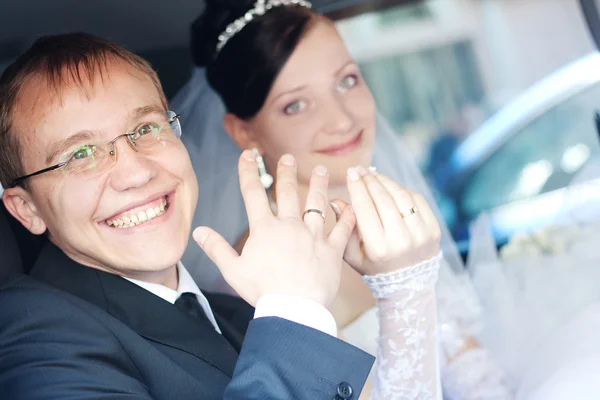 Улыбающаяся пара в машине, держащаяся за руки с кольцами на пальцах — стоковое фото