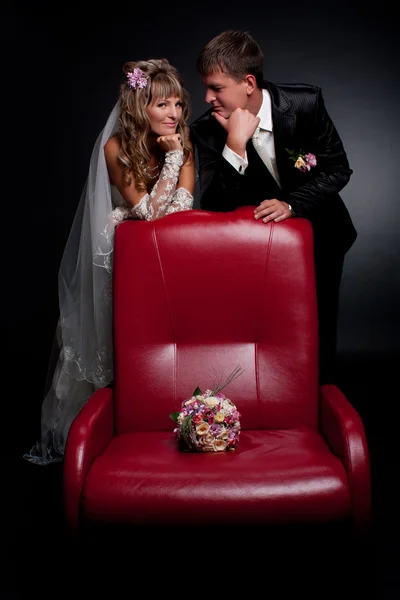 Счастливая пара у красного стула в студии — стоковое фото