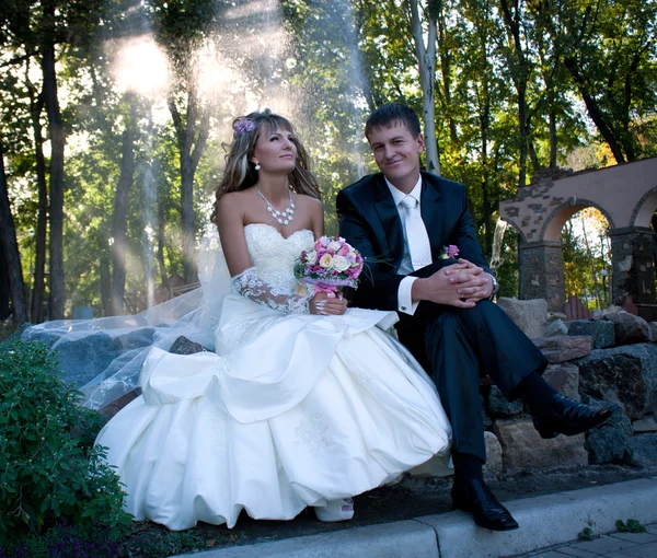 The newlyweds sitting on the rock in the park — Stock Photo, Image