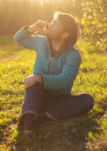 Мужчина сидит на траве и пользуется мобильным телефоном — стоковое фото