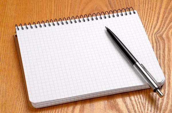 Un cuaderno blanco con bolígrafo negro sobre mesa de madera — Foto de Stock