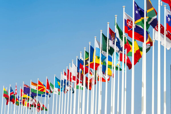 Many world flags flying in a row outside of expo center in 2020 waving on blue sky background.