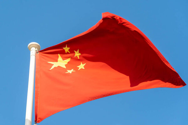 China Flag hanging and blowing in sunshine on blue sky background.
