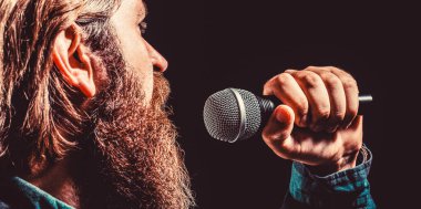 Erkek, mikrofonla şarkı söylüyor. Elinde mikrofon olan ve şarkı söyleyen sakallı bir adam. Karaokedeki sakallı adam mikrofona şarkı söylüyor. Erkek karaokeye katılıyor