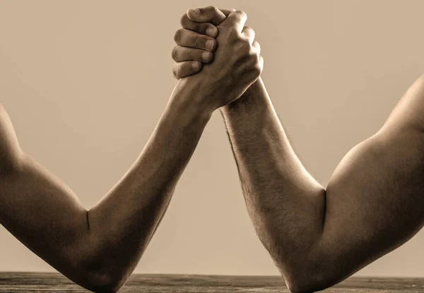 Arm wrestling. Heavily muscled man arm wrestling a puny weak man. Arms wrestling thin hand and a big strong arm in studio. Two mans hands clasped arm wrestling, strong and weak, unequal match Stock Picture