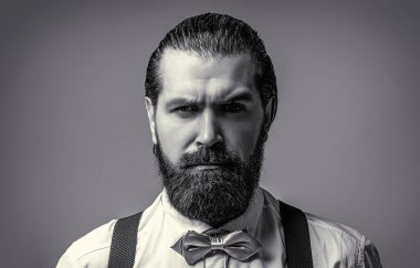 Beyaz gömlek, papyon ve pantolon askısı takmış sakallı yakışıklı bir adamın portresi. Bir beyefendinin papyonuna yakın çekim. Papyonlu ve askılı sakallı adam. Renkli kravatını düzelten gömlekli bir erkek.