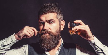 Sakallı adam elinde brendi bardağı tutuyor. Tatma ve degukasyon konsepti. Zarif takım elbiseli sakallı bir işadamı ve bir bardak viski. Viski, konyak, konyak içen bir adam. Degukasyon, tatma