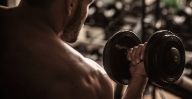 Vücut geliştirici, dambıllarla egzersiz yapıyor. Vücut geliştirici spor salonunda halterlerle çalışıyor.