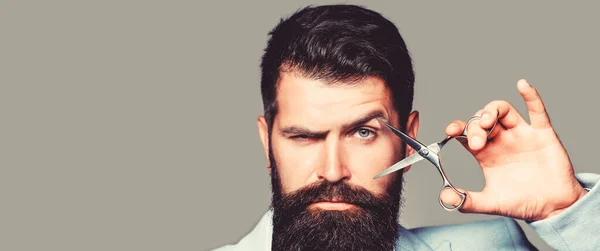 Tijeras de peluquería, peluquería. Hombre brutal, bigote. Varón en peluquería, corte de pelo, afeitado. Corte de pelo de hombre en la peluquería. Hombre barbudo aislado sobre fondo gris y blanco. Copiar espacio —  Fotos de Stock