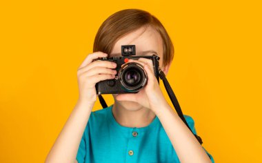 Eski model bir kamera kullanarak fotoğraf çeken küçük bir çocuk. Stüdyodaki çocuk profesyonel kamerayla. Kamera kullanan bir çocuk. Kameralı bebek. Neşeli gülümseyen çocuk elinde kamerayla