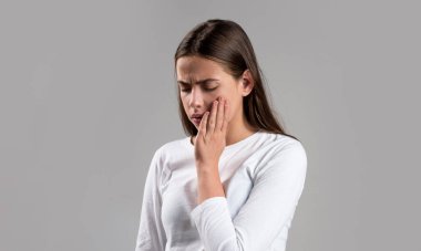 Diş ağrısı, diş çürüğü ya da hassasiyet çeken bir kız. Diş ağrısı, diş enfeksiyonu olan kadın. Gri arka planda diş ağrısı çeken bir kadın. Diş ağrısı çeken genç bir kadın.