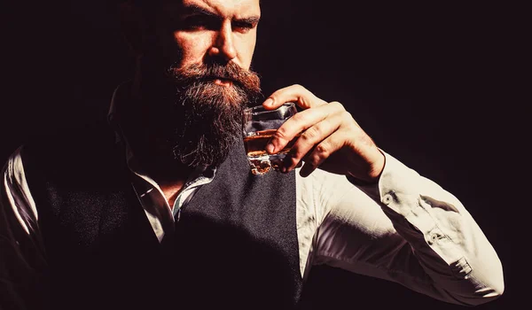 Atrakcyjny mężczyzna z whiskey. Przystojny brodaty mężczyzna ze stylowymi wąsami i brodą pijący brandy lub whiskey ze szkła — Zdjęcie stockowe