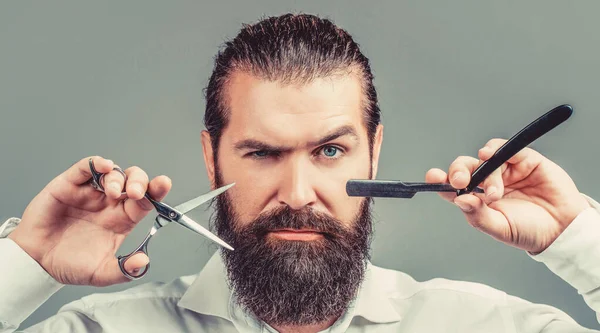 Tipo brutal, tijeras, navaja de afeitar. Cliente barbudo visitando peluquería. Tijeras de peluquero y navaja de afeitar, peluquería, traje. Peluquería vintage, afeitado. Hombre barbudo retrato. Hombres bigote —  Fotos de Stock