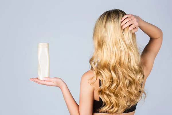 Cabelo longo de mulher. Mulher segurar shampoo garrafa e condicionador. Mulher segurando garrafa de xampu. Menina loira bonita com uma garrafa de shampoos nas mãos. Menina com cabelo brilhante e longo — Fotografia de Stock