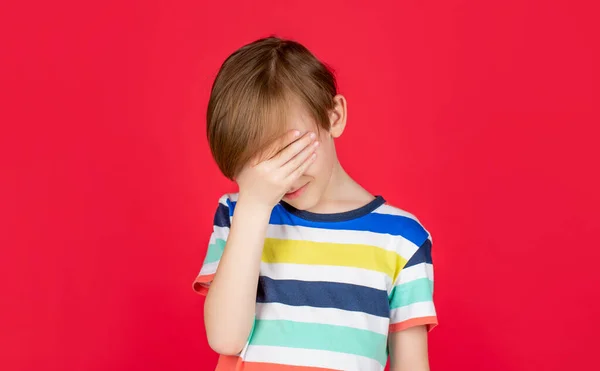 Portrait of a sad boy holding his head with his hand, isolated on the red background. Little boy having a headache. Despair, tragedy. Headache child. Suffering migraine. Headache because stress — Stock Photo, Image
