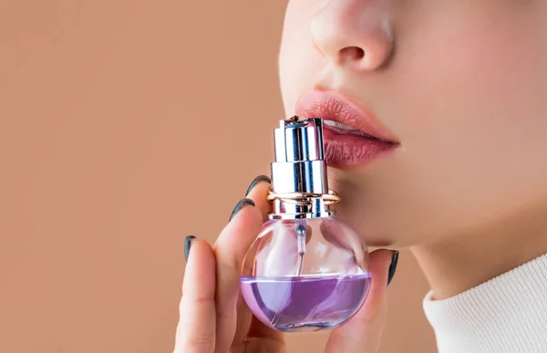 Beautiful girl using perfume. Woman with bottle of perfume. Woman presents perfumes fragrance. Sexy lips. Pink lip. Close up of sexy plump soft lips with dark red lipstick
